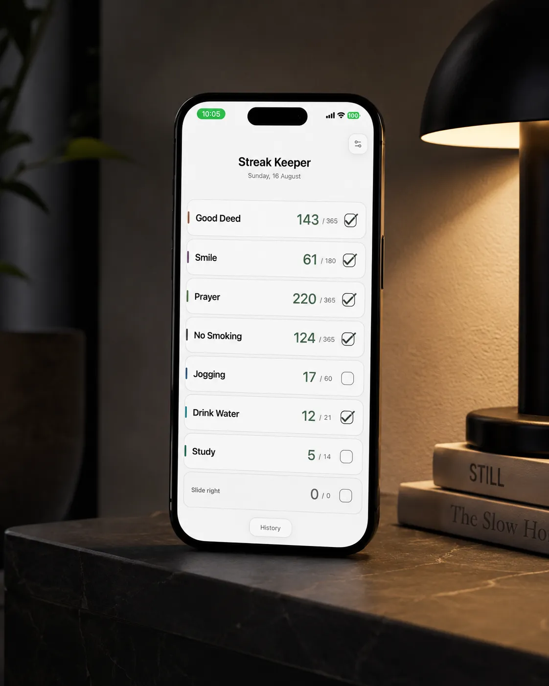 The Streak Keeper home screen at night, showing six named daily streaks with running counts, most checked off for the day, on an iPhone beside a lit bedside lamp.